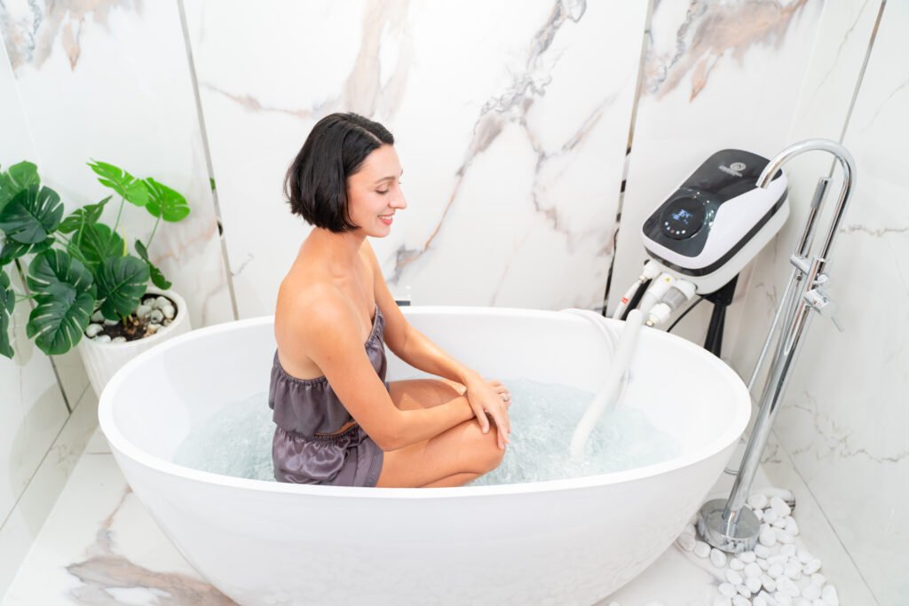 Onsena SPA - Máy Tắm Thủy Liệu Khoáng Nóng Onsen Nhật Bản 98 Người phụ nữ thư giãn trong bồn tắm với máy tạo bọt, không gian phòng tắm trang nhã và cây xanh tươi tốt.
