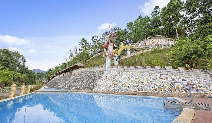 Hồ bơi xanh mát với tượng rồng trên đồi, dưới bầu trời trong xanh, tạo nên khung cảnh yên bình và hài hòa.