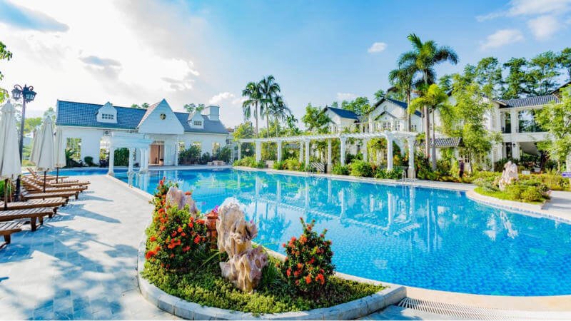 Hồ bơi ngoài trời xanh biếc tại resort sang trọng với hàng cây xanh và ghế dài thư giãn dưới ánh nắng.