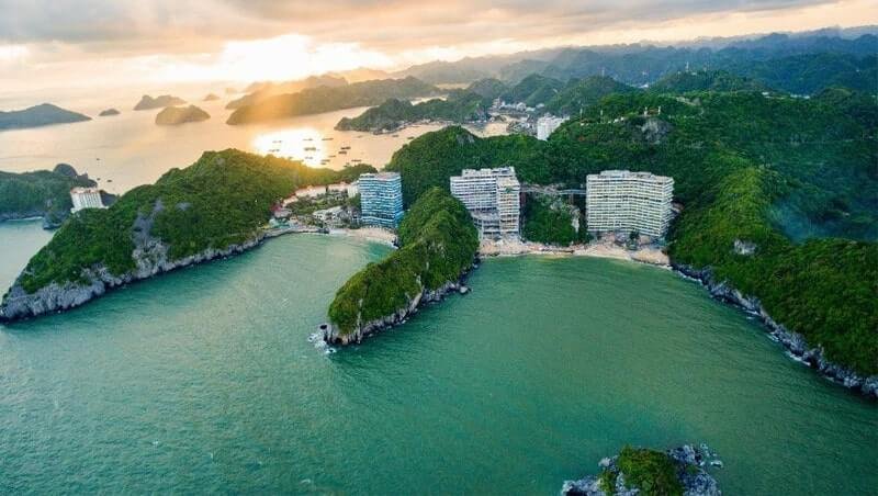 Vịnh Hạ Long với đảo xanh mát và toà nhà dọc bờ biển trong ánh hoàng hôn, tạo cảnh quan tuyệt đẹp từ trên cao.