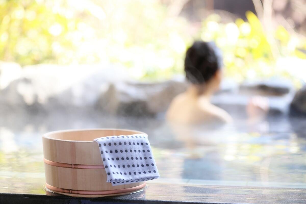 Người thư giãn trong suối nước nóng với thùng gỗ và khăn trên bờ. Spa ngoài trời, phong cảnh tự nhiên.