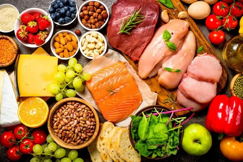 Thực phẩm lành mạnh gồm rau, trái cây, thịt, cá hồi, hạt và phô mai trên mặt bàn.