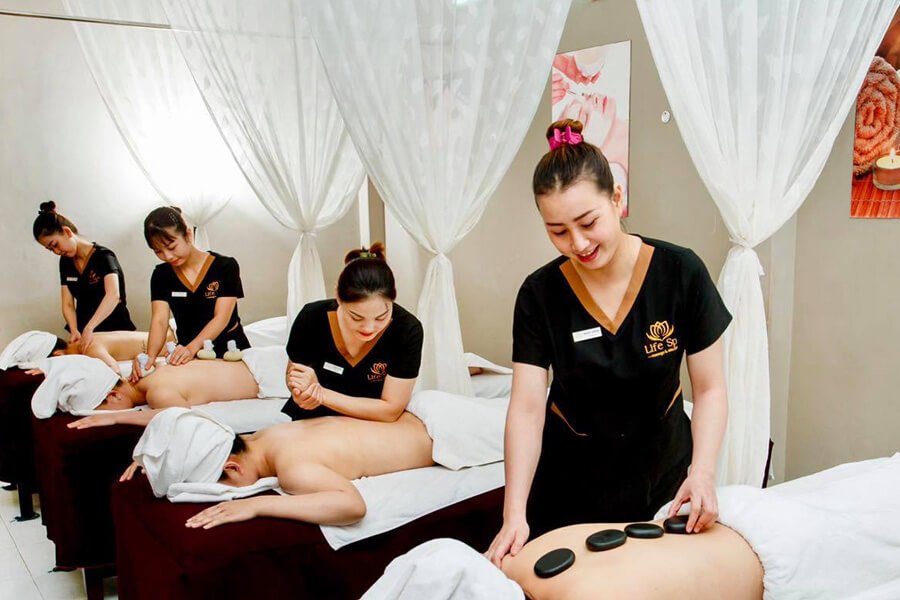 Nhân viên massage spa chuyên nghiệp đang thực hiện trị liệu với đá nóng cho khách hàng trong phòng thư giãn.