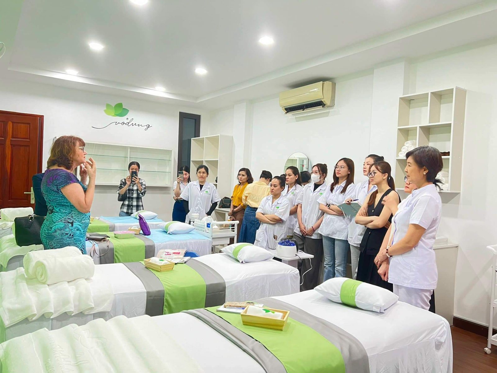 Buổi hướng dẫn tại spa với giường massage và học viên trong trang phục chuyên nghiệp.