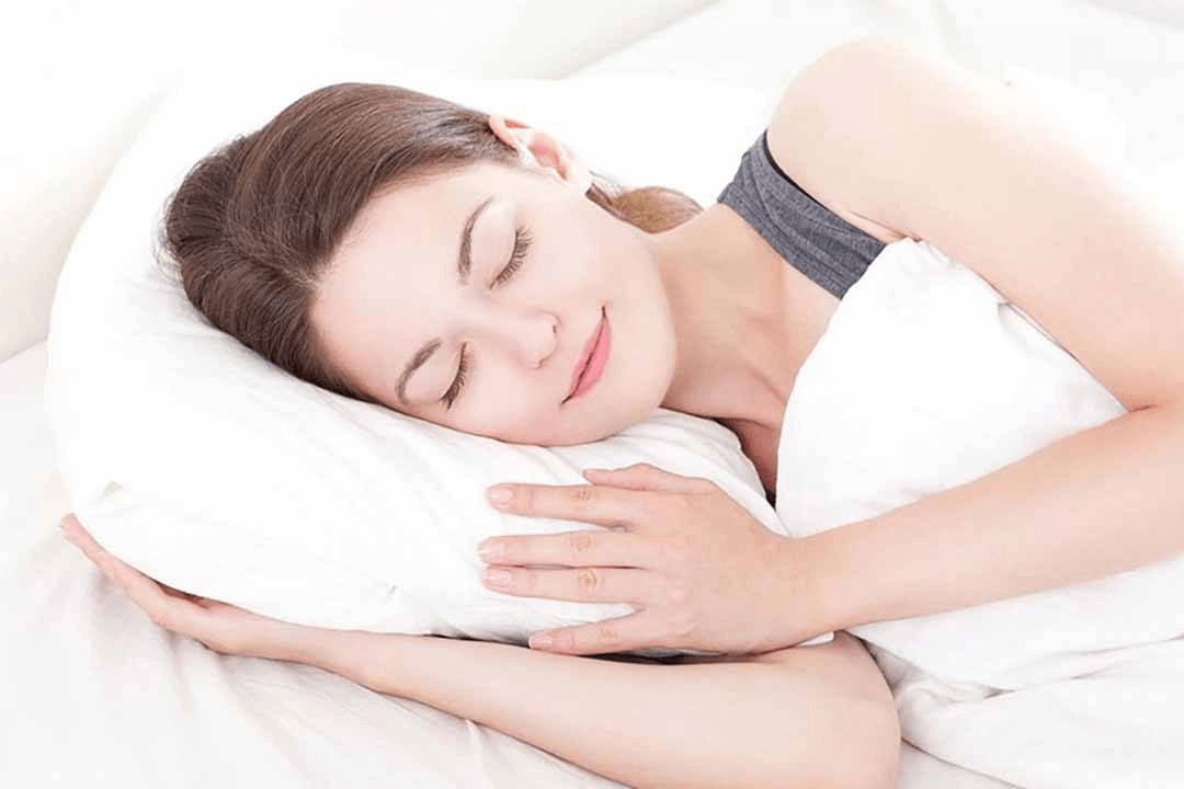 Người phụ nữ ngủ say giấc trên giường, tựa đầu vào gối trắng, biểu tượng cho giấc ngủ an lành và thư giãn.