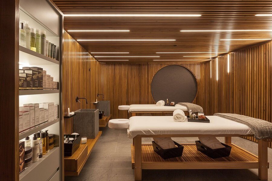 Phòng spa với giường massage đôi và kệ sản phẩm chăm sóc da, thiết kế nội thất gỗ sang trọng.