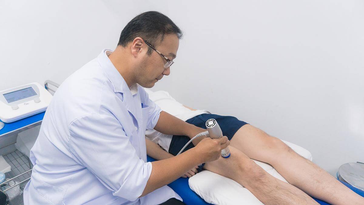 Bác sĩ điều trị bằng liệu pháp sóng xung kích cho bệnh nhân bị đau chân trong phòng khám.