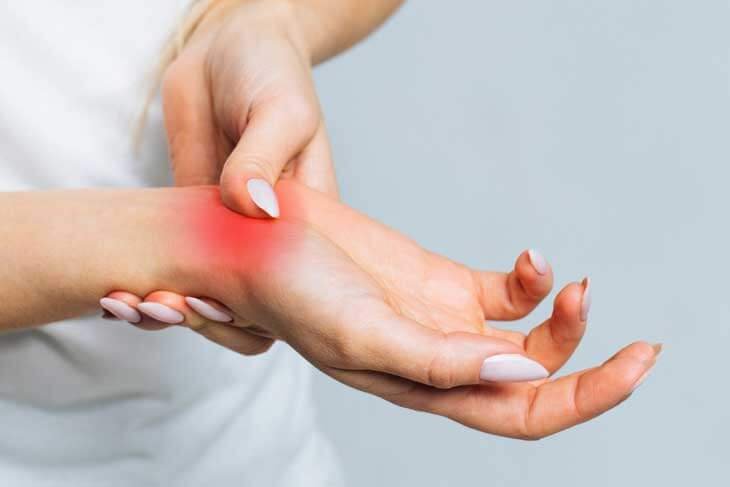 Người cầm cổ tay bị đau, vùng da ửng đỏ, thể hiện triệu chứng viêm khớp hoặc đau cơ.