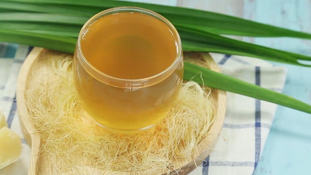 Ly nước mát làm từ râu ngô và lá dứa, trang trí trên bàn gỗ.