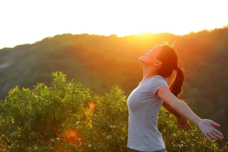 Người phụ nữ trong ánh nắng mặt trời, dang tay đón nhận thiên nhiên trước núi xanh tươi.
