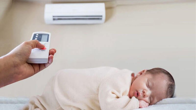 Em bé ngủ ngon dưới máy lạnh với điều khiển từ xa, tạo không gian thoải mái và yên tĩnh cho giấc ngủ.
