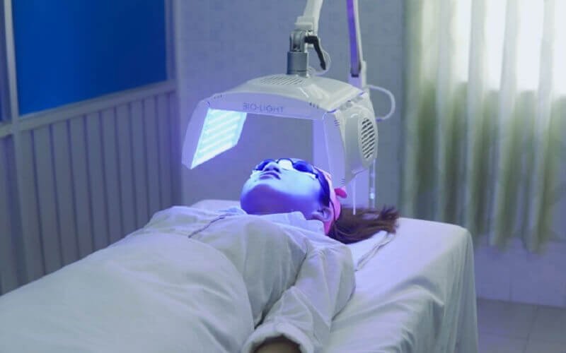Người phụ nữ trị liệu da mặt bằng ánh sáng LED xanh trong spa.