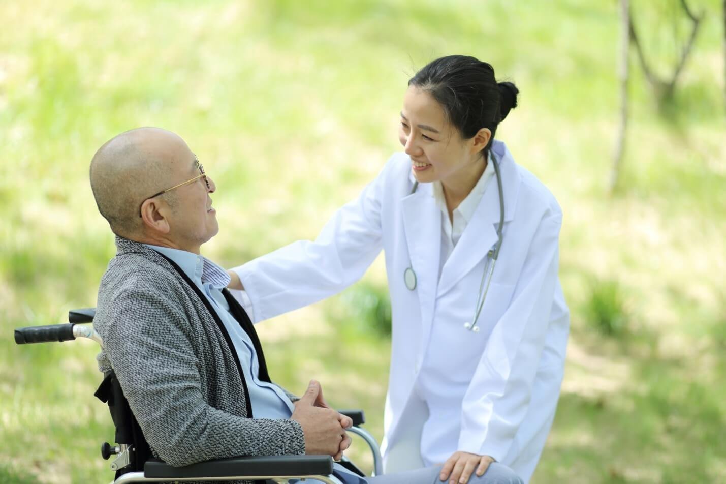 Bác sĩ trò chuyện với một người ngồi xe lăn trong khung cảnh ngoài trời, cả hai đều mỉm cười.