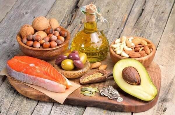 Thực phẩm giàu omega-3: cá hồi, bơ, dầu ô liu, các loại hạt và quả hạch trên bàn gỗ.