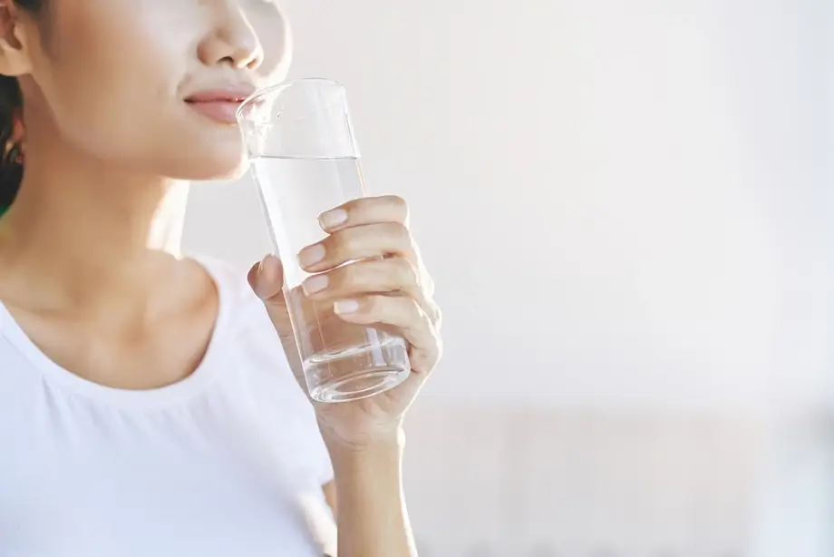 Người phụ nữ uống nước từ ly thủy tinh, giữ sức khỏe và bổ sung đủ nước.
