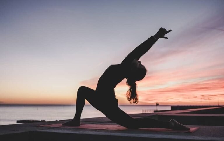 Người tập yoga tại bình minh trên bãi biển, thực hiện động tác uốn cong cơ thể trên thảm.