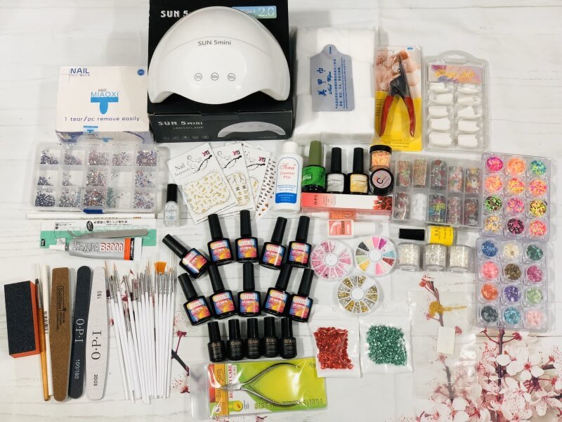 Bộ dụng cụ làm móng đầy đủ với đèn UV, lọ sơn, phụ kiện nail và dụng cụ chăm sóc, bố trí trên bàn trắng.
