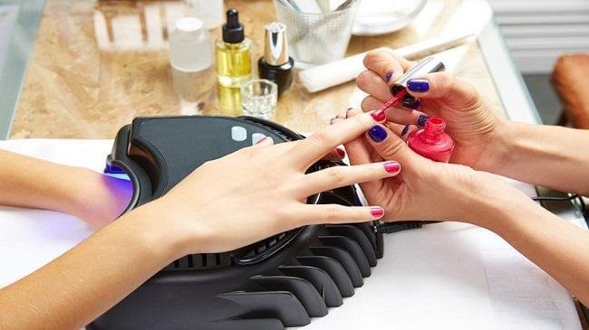 Sơn móng tay tại tiệm làm móng, dùng cọ sơn màu hồng, chăm sóc sắc đẹp chuyên nghiệp.