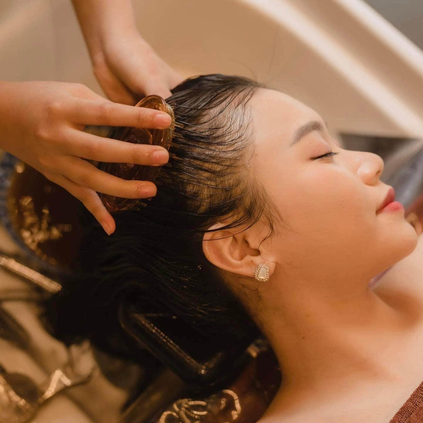 Người phụ nữ thư giãn khi được mát-xa da đầu tại tiệm salon, tạo cảm giác thư thái và chăm sóc tóc.