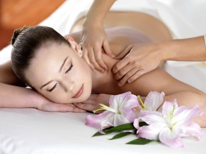 Người phụ nữ thư giãn với liệu pháp massage cùng hoa ly bên cạnh.