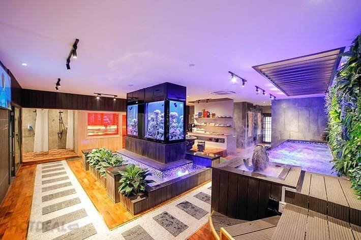 Phòng spa hiện đại với bể cá lớn, tường cây xanh và bồn tắm nước nóng, ánh sáng ấm áp và nội thất gỗ.