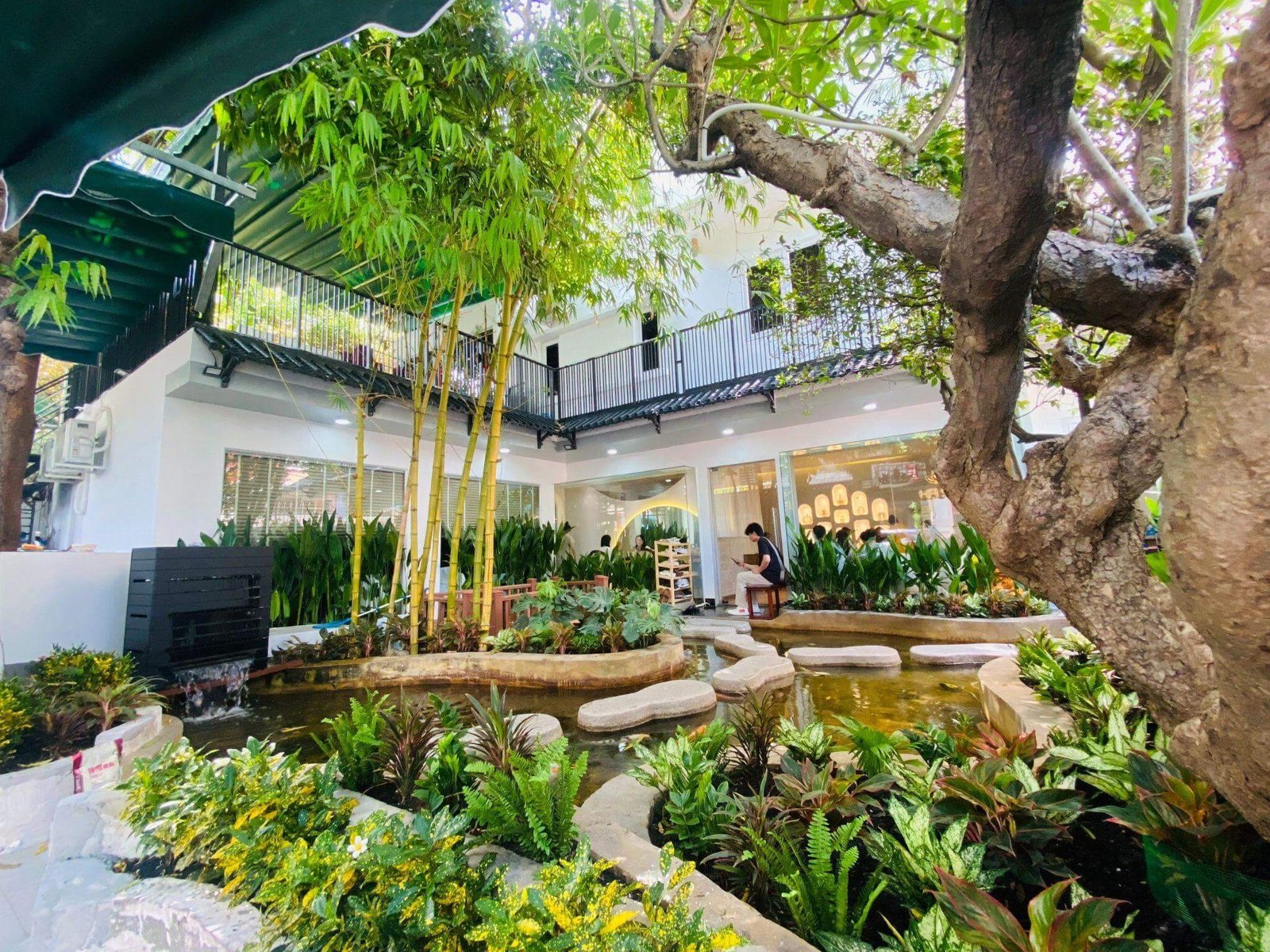 Khu vườn nhỏ với ao nước, cây cối xanh tươi và quán cà phê thư giãn phía trong.