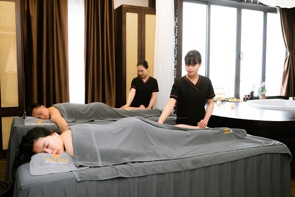 Hai khách hàng được massage thư giãn tại spa, nhân viên đang thực hiện liệu pháp chăm sóc chuyên nghiệp.