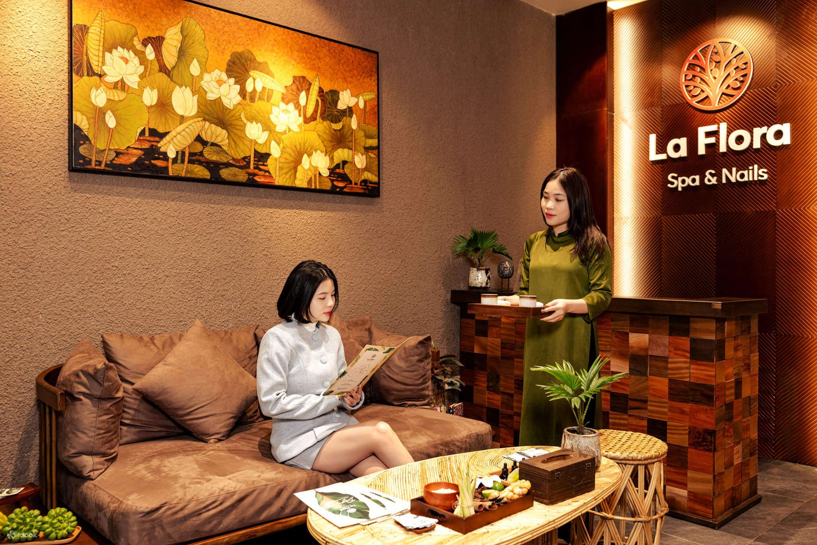 Khách ngồi ghế sofa tại La Flora Spa & Nails, thư giãn cùng bảng menu. Nội thất spa ấm cúng và trang trí đặc sắc.