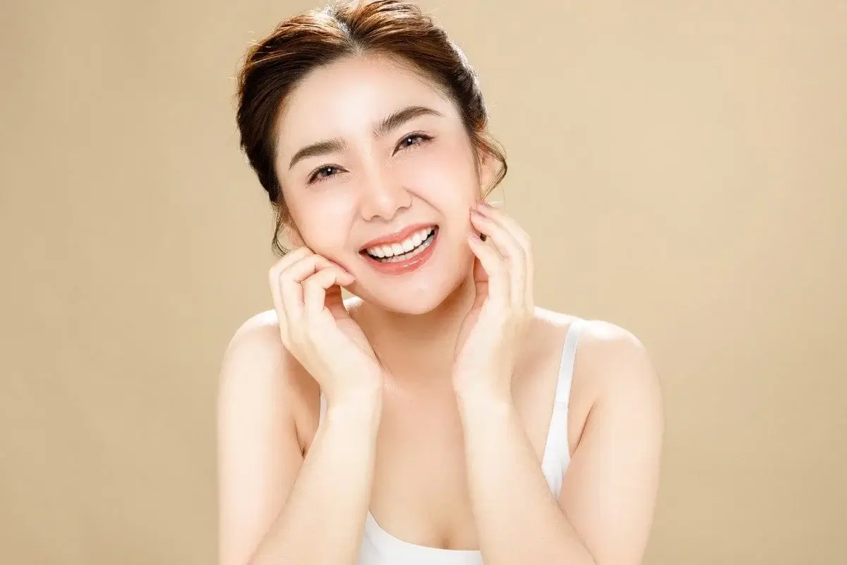 Người phụ nữ cười rạng rỡ, chạm tay vào mặt, nền màu be, phong cách tươi sáng.