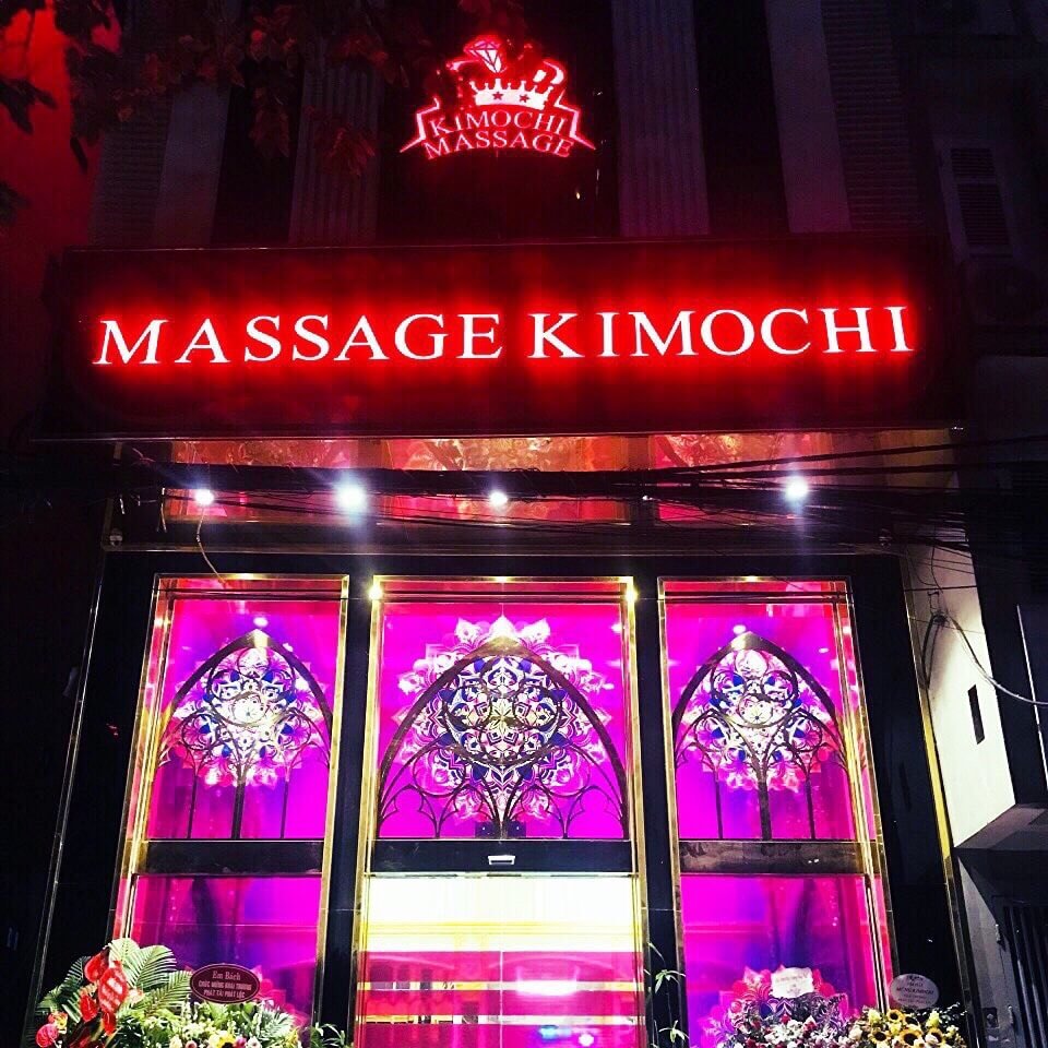 Biển hiệu Massage Kimochi đỏ rực, nổi bật trên nền cửa sổ kính trang trí hoa văn, ánh sáng tím lung linh.