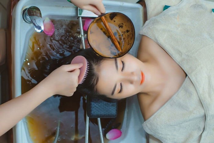 Người phụ nữ thư giãn gội đầu dưỡng chất tại spa, tận hưởng không gian thư giãn với nước thảo dược.