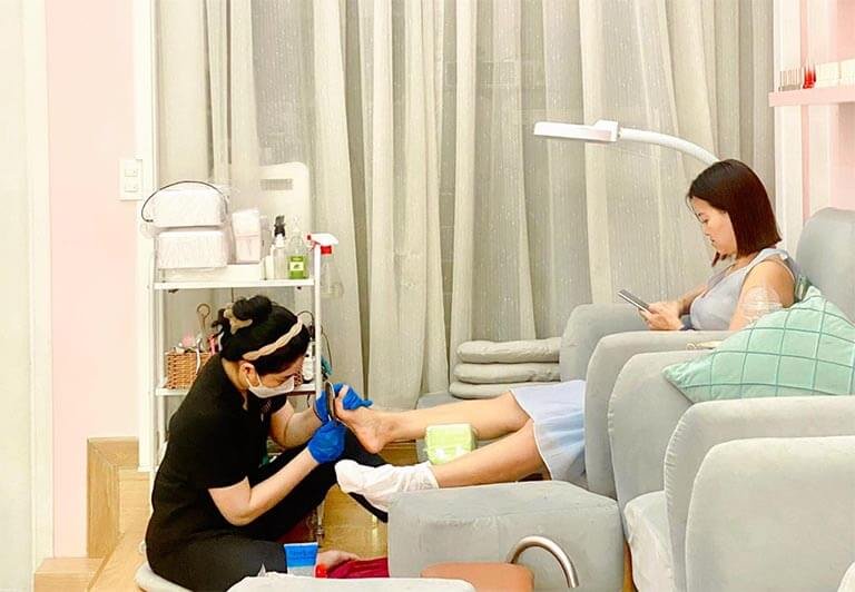 Nhân viên làm móng chân cho khách thư giãn trong tiệm, không gian thoải mái và sáng sủa.