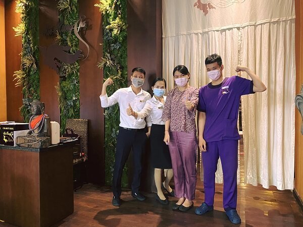 Nhóm bốn người đeo khẩu trang đứng trong môi trường nội thất với trang trí cây xanh, tạo dáng vui vẻ.