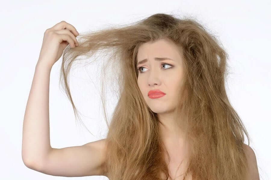 Người phụ nữ lo lắng nhìn tóc hư tổn và rối xù, biểu cảm không hài lòng.