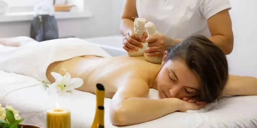 Người phụ nữ thư giãn trong spa với liệu pháp massage thảo dược, không gian ấm cúng với nến và hoa trang trí.