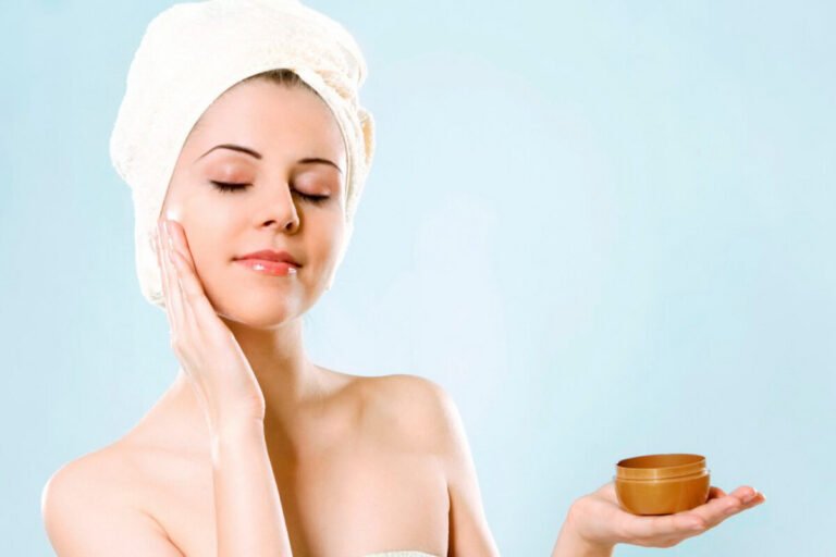 Người phụ nữ quấn khăn, thoa kem dưỡng lên mặt, tạo cảm giác thư giãn trên nền xanh.