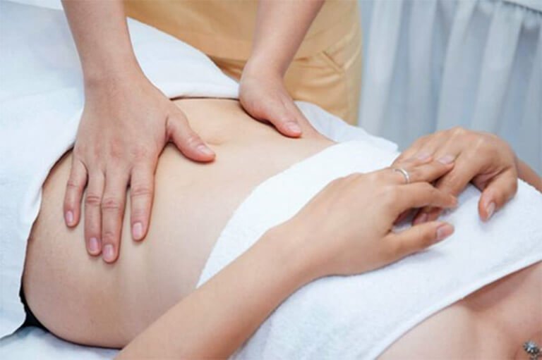 Nhân viên massage đang xoa bóp vùng bụng cho khách hàng trong spa thư giãn.