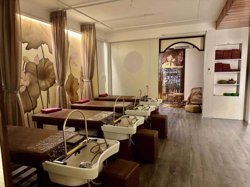 Phòng spa thư giãn với ghế và bồn rửa thiết kế sang trọng, tông màu nâu ấm áp, tranh hoa sen nghệ thuật.