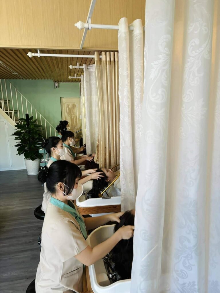Nhân viên chăm sóc tóc gội đầu cho khách hàng trong spa, thể hiện dịch vụ chất lượng và thư giãn.