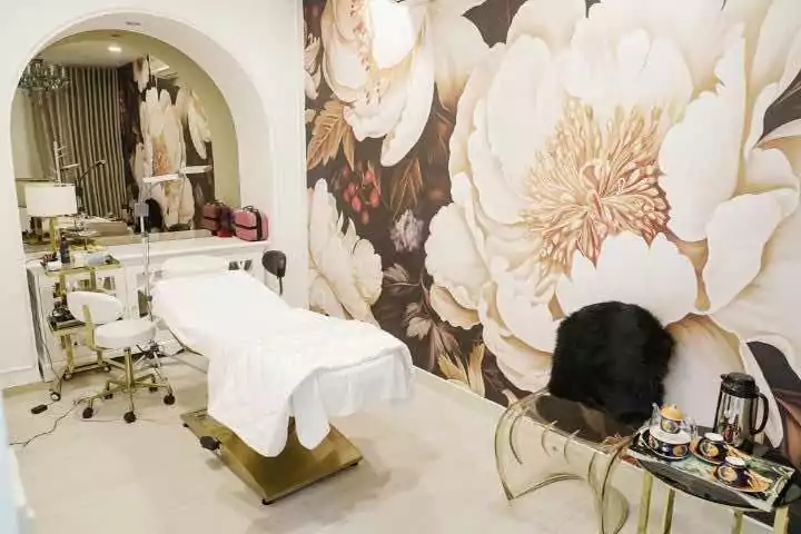 Phòng spa sang trọng với tranh tường hoa lớn, giường trị liệu và bàn nhỏ trang trí.