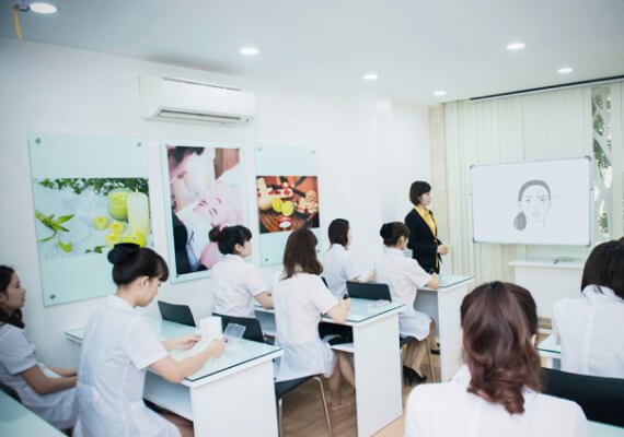 Nhóm học viên trong lớp học chăm sóc da, giảng viên đang thuyết trình trước bảng trắng.