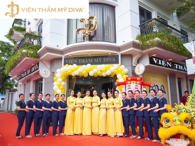 Nhân viên Viện Thẩm Mỹ Diva trong trang phục áo dài vàng, đứng trước cửa viện với trang trí bóng bay và múa lân.
