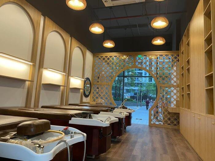 Salon tóc hiện đại với nội thất gỗ, bồn gội đầu, trang trí đèn thả và cửa sổ lớn hình tròn.