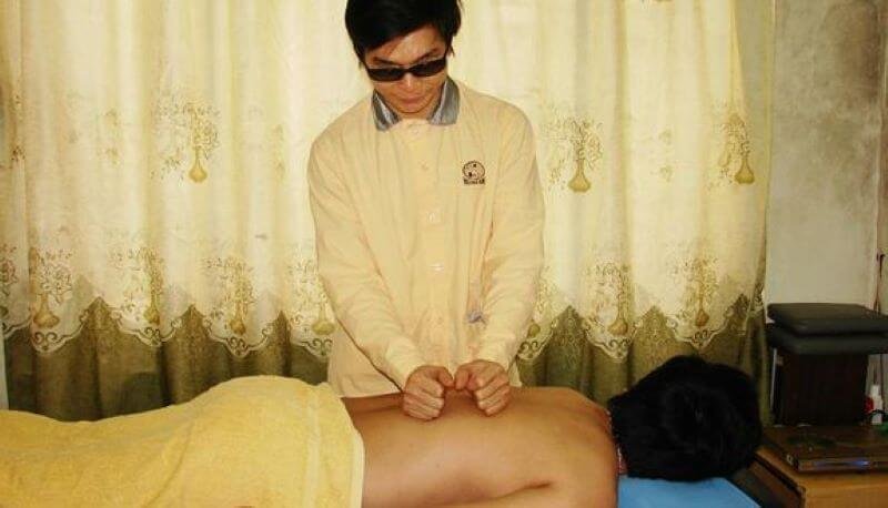 Kỹ thuật viên mát-xa thực hiện liệu pháp mát-xa lưng trong phòng có rèm vàng, mang lại sự thư giãn và phục hồi.