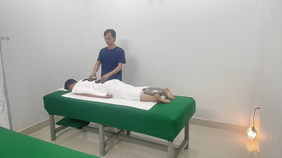 Người đàn ông đang thực hiện liệu pháp bấm huyệt cho khách hàng nằm trên giường massage trong phòng trị liệu.