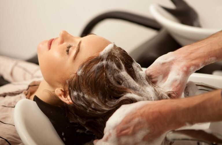 Người phụ nữ đang được gội đầu tại tiệm salon, tóc đầy bọt xà phòng, thư giãn trên ghế ngồi.