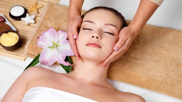 Người phụ nữ thư giãn với trị liệu massage mặt, có hoa, kem dưỡng da và khăn bông spa.
