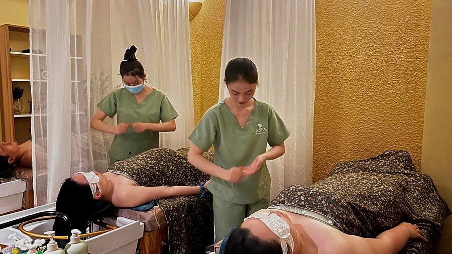 Nhân viên spa đang thực hiện liệu pháp massage cho hai khách hàng trong phòng với ánh sáng ấm áp.