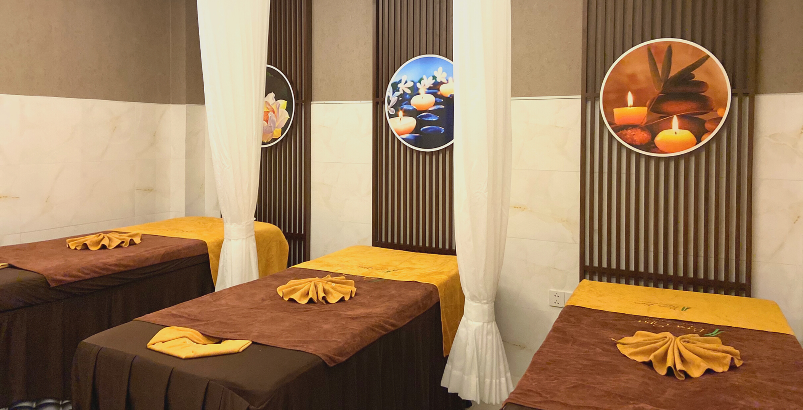 Phòng spa thư giãn với ba giường mát-xa trang trí khăn xếp đẹp và nến tạo không gian thư thái.