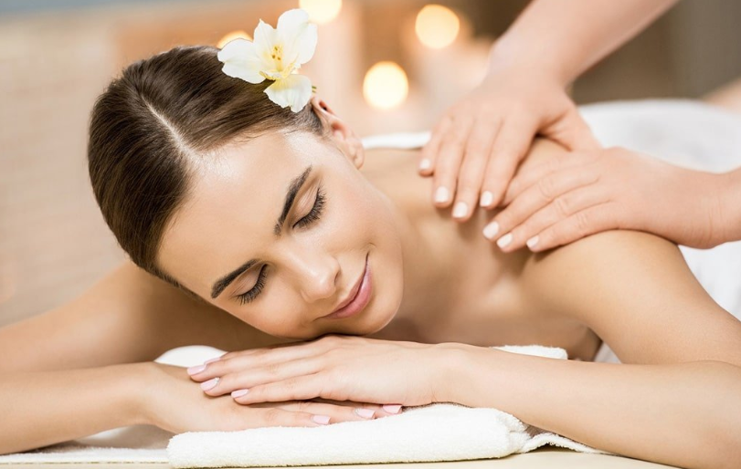 Người phụ nữ thư giãn khi được massage tại spa, tóc cài hoa trắng, ánh sáng dịu nhẹ.
